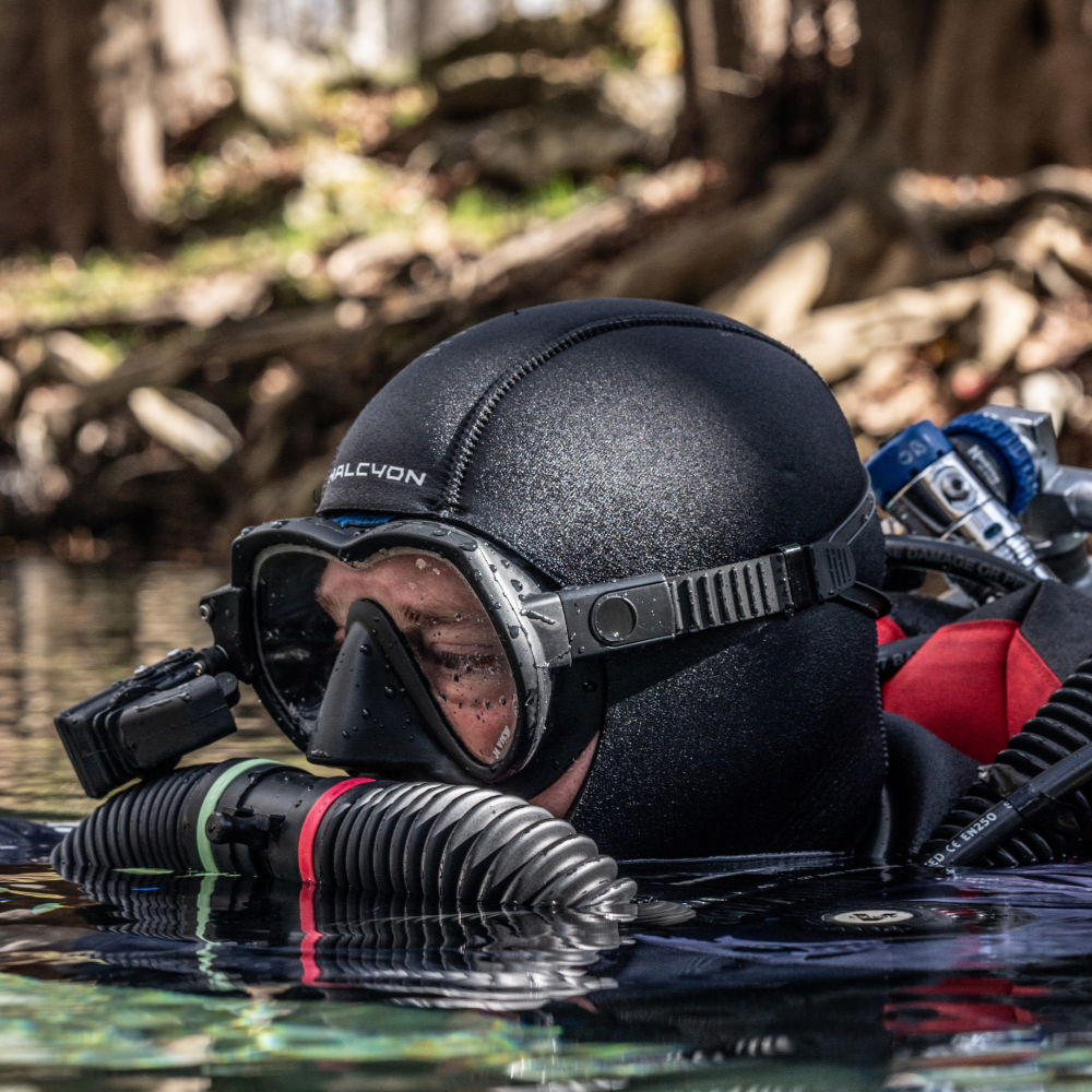 Person scuba diving in a natural water setting with trees in the background